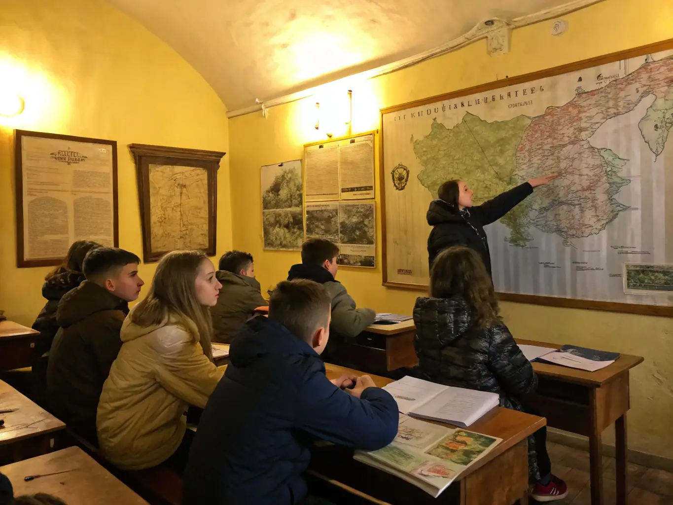 A detailed photo of students and teachers exploring archival documents and artifacts in a classroom, with educational posters about local history on the walls.